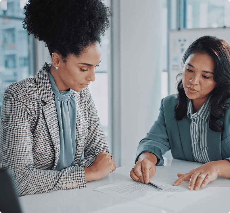 Two women sitting at a table with papers.