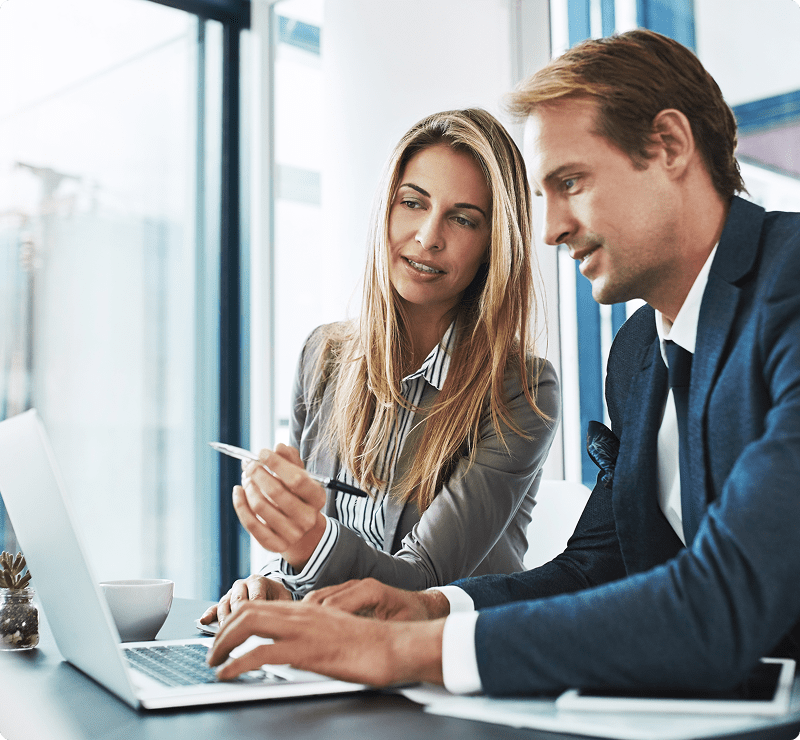 A man and woman sitting at a table looking at a laptop.